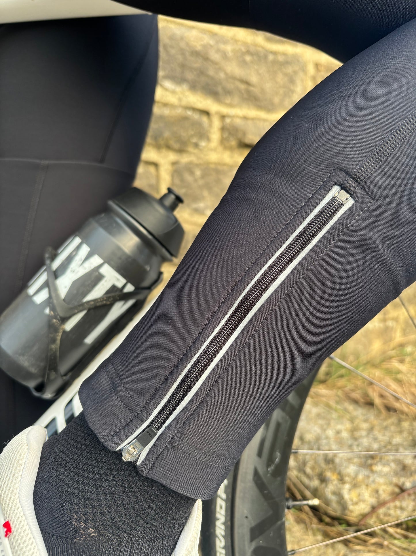 Close-up of black women's cycling bib tights showing the lower-leg fit and reflective detailing beside a bicycle.